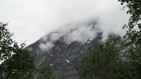 Norwegian mountain covered in clouds with greenery in the foreground Stock Footage 243886592