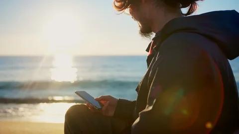 Nostalgic millennial using smartphone internet app in loneliness in sunrise sky Stock Footage 100896736