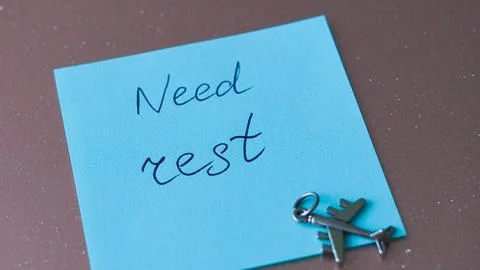 Note on blue sticky pad with text about needing rest and airplane charm Stock Photos