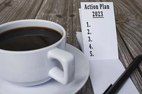 Note book with action plan 2023 text and coffee on wooden desk. Stock Photos