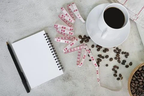 Note book with cup of coffee, coffee beans background and measure tap. Stock Photos