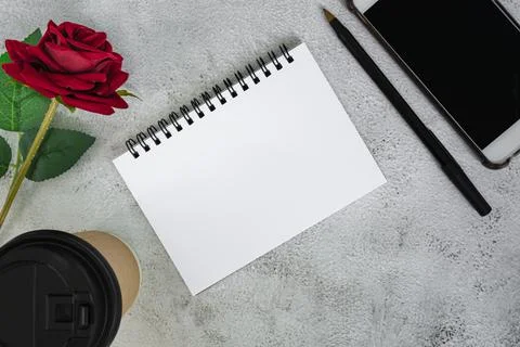 Note book with disposable coffee cup, pen, smartphone and roses on marble tab Stock Photos