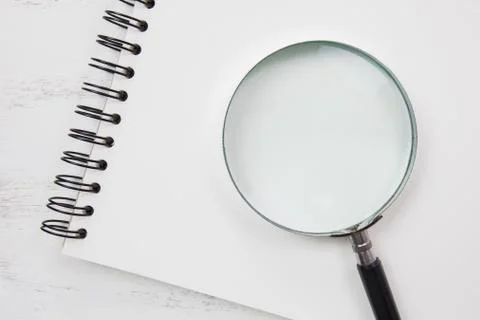 Note book on white table with magnifying glass Stock Photos