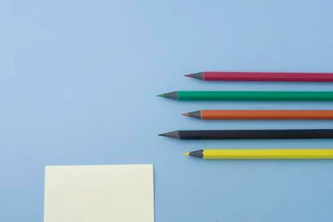 Note with multicolored pencils isolated on light blue, pastel table. Space fo Stock Photos