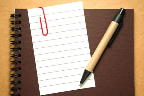 Note paper clip on notebook with pen on brown cardboard background Stock Photos
