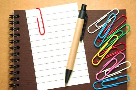 Note paper clip on notebook with pen and colorful paperclips on brown cardboa 库存照片