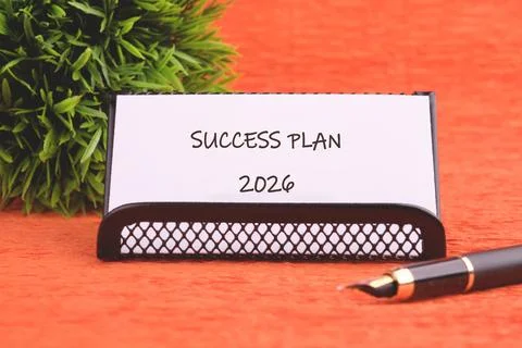 A note reading Success Plan 2026 sits in a holder, with a pen to its side and Stock Photos