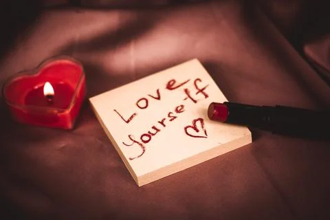 A note to self with a call to love yourself drawing with red lipstick Red candle Foto stock