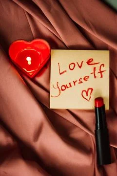 A note with text love yourself drawing with red lipstick on a silk terracote Foto stock