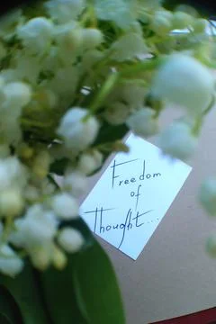 Note with text on white paper and blurred bouquet of lilies of the valley Stock Photos