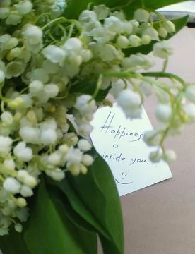 Note with text on white paper and blurred bouquet of lilies of the valley Stock Photos