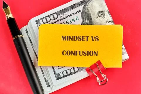 A note with the words mindset vs confusion sits on top of a stack of cash alo Stock Photos