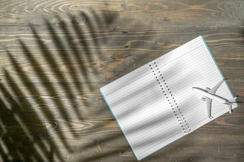 Notebook and airplane with the shadow of a palm leaf on a wooden table. Moc.. Stock Photos