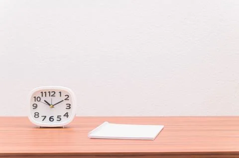 The notebook and the clock are on the table. Stock Photos