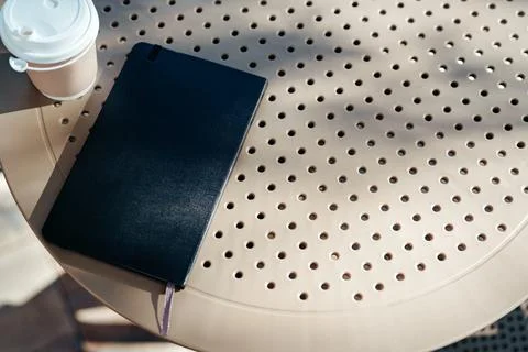 Notebook and coffee cup resting on a round table in a sunny outdoor cafe setting Stock Photos