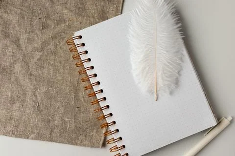 Notebook and feather on a light surface beside a piece of fabric in a quiet 스톡 사진