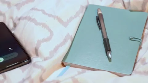 Notebook and pen on bed and an incoming call from work Stock Footage 150283343