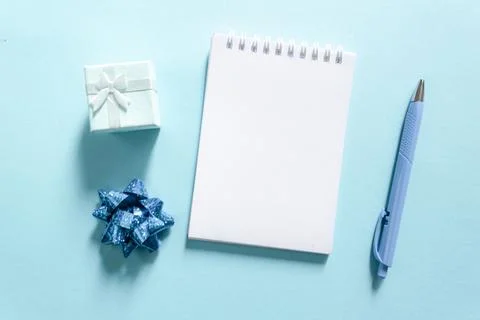 Notebook and pen on a blue background, spiral notepad with gift on a table. s Stock Photos