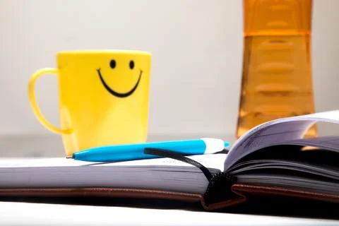 Notebook and pen on the table to write down notes with a smiling-faced cup. Stock Photos