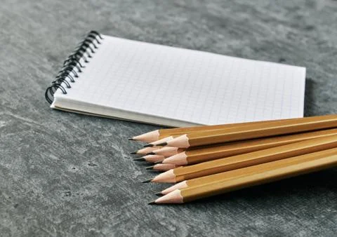 Notebook and stack of simple golden colored pencils on gray background, shall Stock Photos
