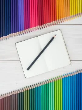 Notebook and two rows of colored pencils on wooden background Foto stock