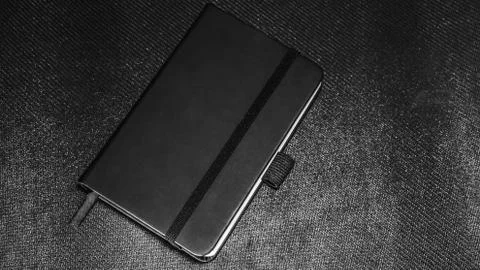 Notebook with black cover on black textured background Stock Photos