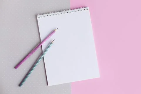 Notebook with blank page and two pencils on a pink and grey background. Flat Foto stock