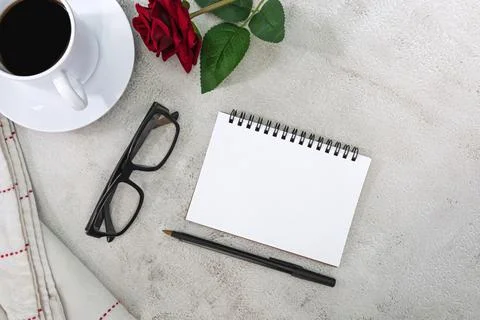 Notebook with coffee, pen, reading glasses, roses on white marble table. Stock Photos