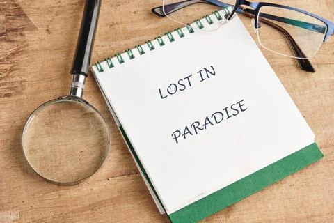 Notebook displaying the phrase Lost in Paradise sits next to a magnifier and Foto stock