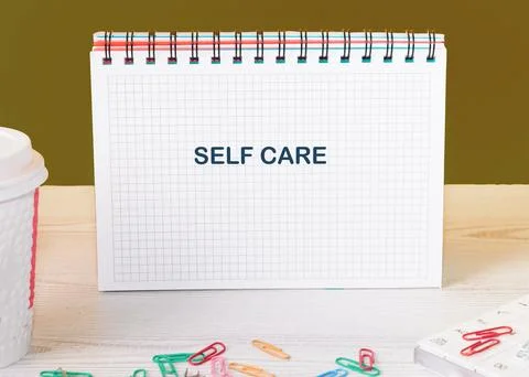 A notebook featuring the words self care lays open on a wooden table, surroun Foto stock