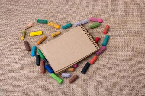 Notebook in the middle of crayons form a heart Stock Photos
