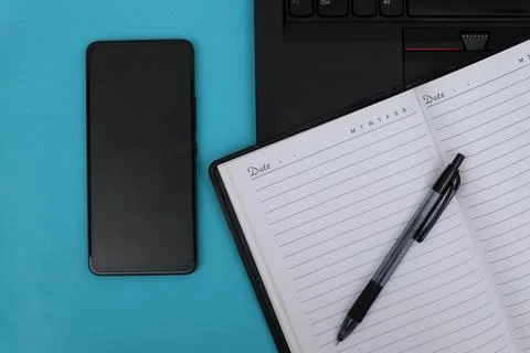 The notebook is open on the laptop next to the smartphone Stock Photos