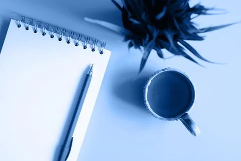 Notebook or sketchbook and a pen and tea cup and green plant on a blue backgr Stock Photos