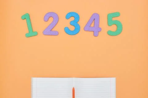 Notebook, pen and colored numbers on orange background. Accessories for study Foto stock