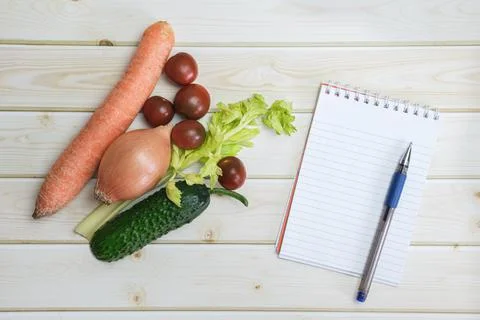 Notebook, pen and different vegetables from the regular diet on the backgroun Stock Photos