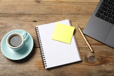 Notebook with pen, sticky note, laptop and coffee on wooden table, above view Stock Photos