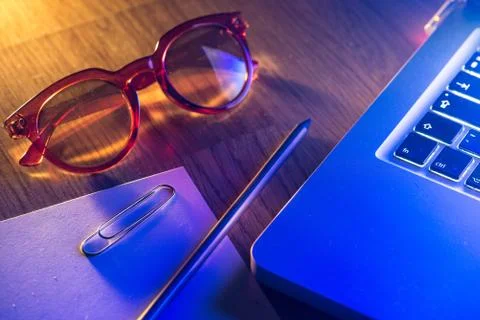 Notebook, pencil, glasses and computer in red and blue light. Stock Photos
