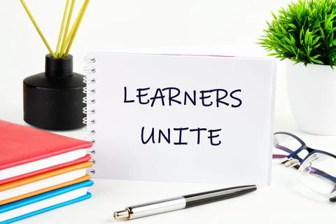 A notebook with the phrase Learners Unite is centered on a desk surrounded by Stock Photos