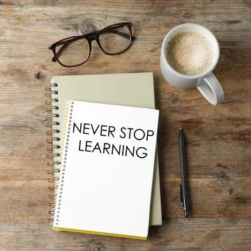Notebook with phrase NEVER STOP LEARNING, glasses and cup of coffee on wooden Foto stock