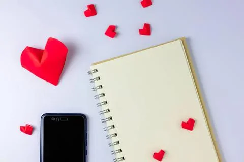 Notebook with red paper hearts and smartphone on light background Stock Photos