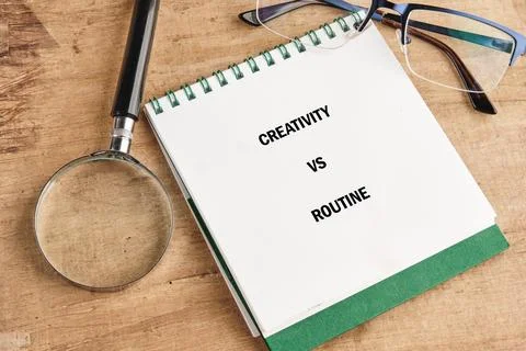 A notebook sits on a wooden table displaying the words creativity vs routine. Fotos Stock
