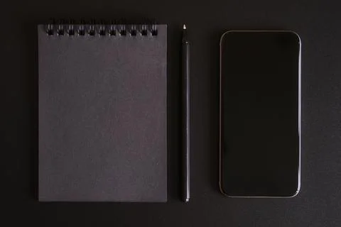 Notebook on a spring with black sheets, and a pen, and mobile phone on a blac Stock Photos