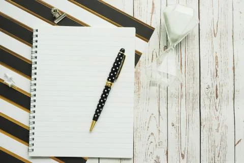 Notebook on a spring, a pen, carnations, a clip and an hourglass on a striped Foto stock