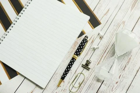 Notebook on a spring, a pen, carnations, a clip and an hourglass on a striped Foto stock
