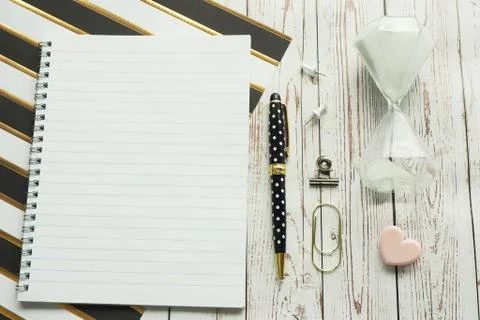 Notebook on a spring, a pen, carnations, a clip and an hourglass on a striped Stock Photos