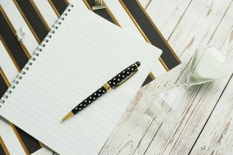Notebook on a spring, a pen, carnations, a clip and an hourglass on a striped Stock Photos