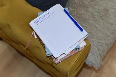 Notebook stack blue pen on yellow upholstered surface, "Homework" word Foto stock