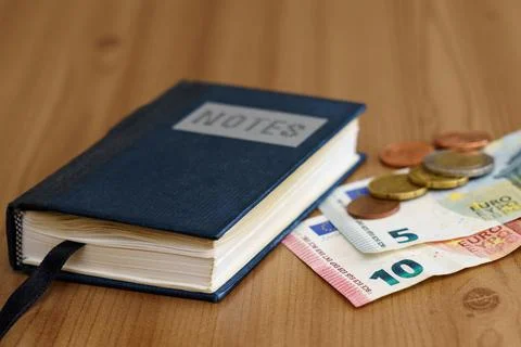 Notebook on the table next to euro banknotes and coins. Stock Photos