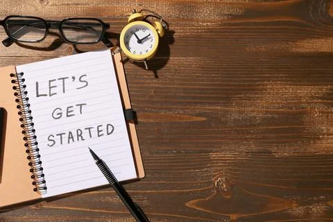 Notebook with text LET'S GET STARTED, alarm clock and eyeglasses on wooden ba Stock Photos