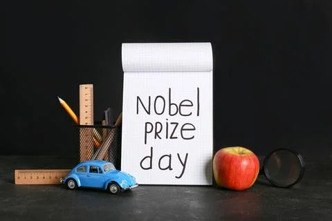 Notebook with text NOBEL PRIZE DAY, apple and stationery on black background Stock Photos